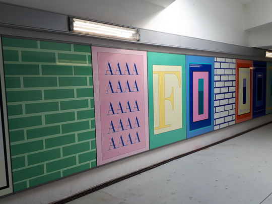 One corridor wall is decorated with colourful panels, including green and white brick patterns, repeated "AAAA" letters in pink and large stylised letters with the word "FOOD" in yellow, red, blue and orange.