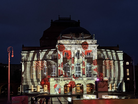 An ornate building is illuminated at night with a colourful projection of red poppies and abstract shapes on its façade, which stands out vividly against the dark sky.