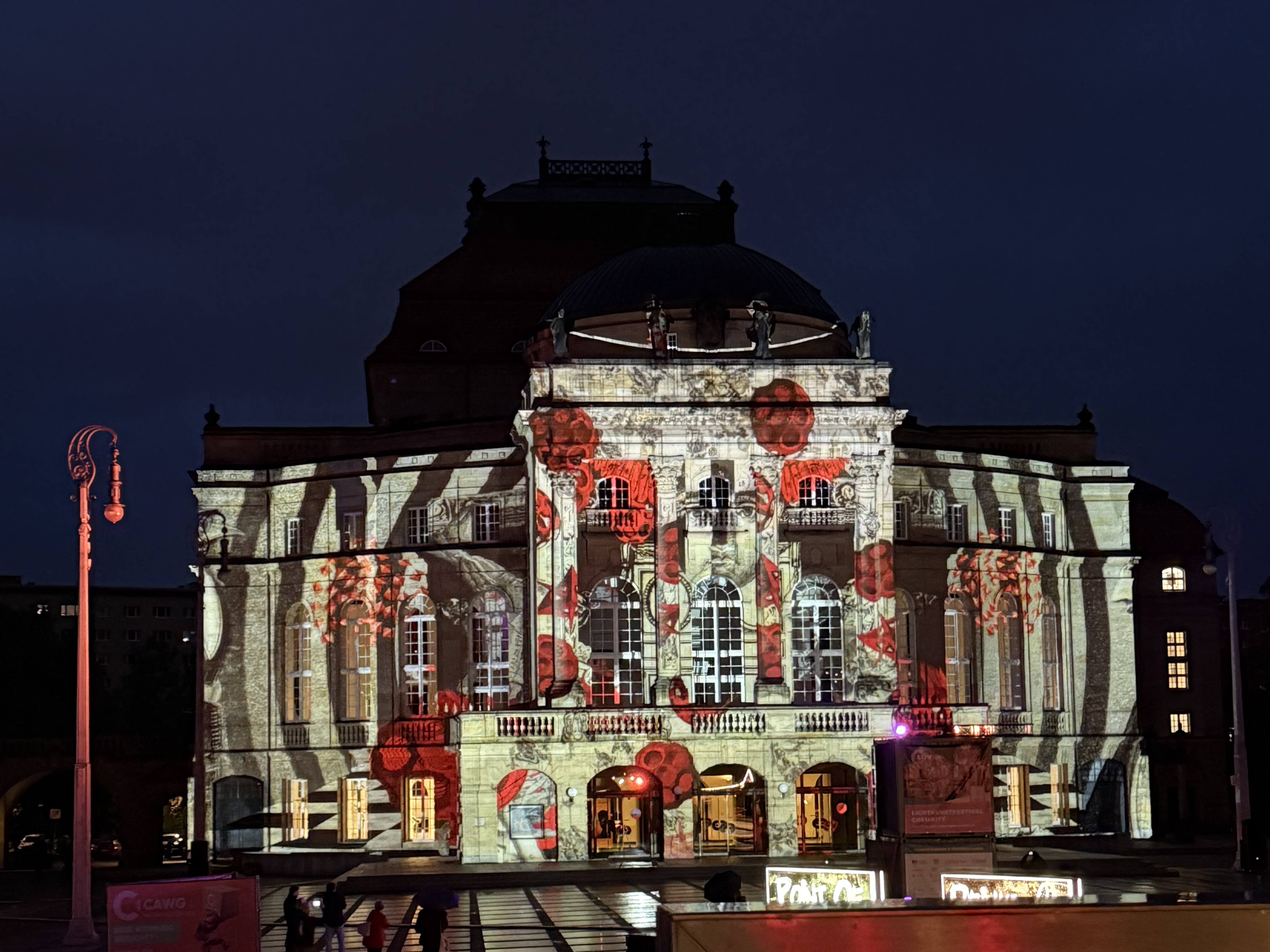 An ornate building is illuminated at night with a colourful projection of red poppies and abstract shapes on its façade, which stands out vividly against the dark sky.
